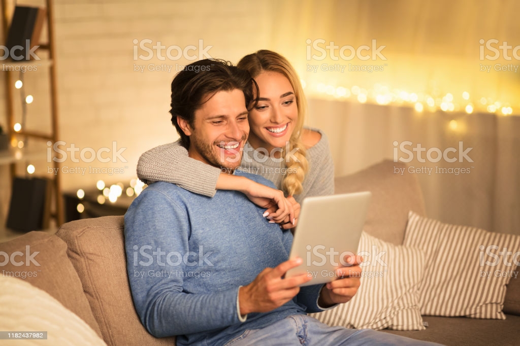 Happy spouses ordering Christmas gifts on tablet, spending winter evening together, free space